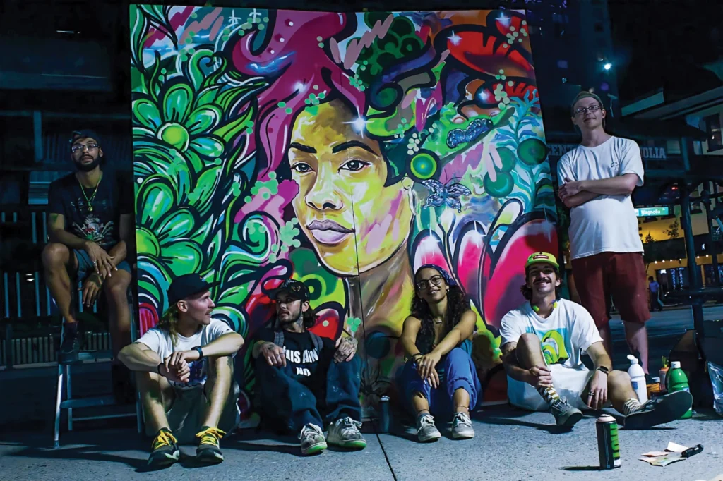 A group of happy people sitting in front of a colorful mural of a person surrounded by nature shapes