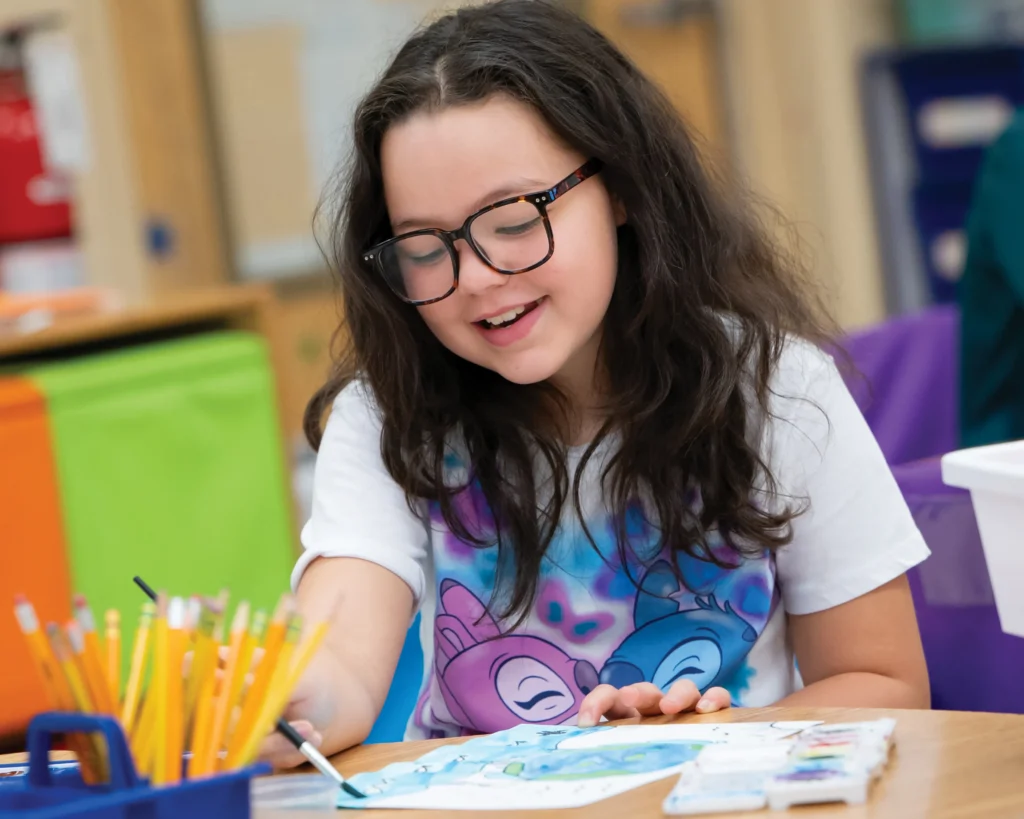 A smiling little girl with glasses works on an art project
