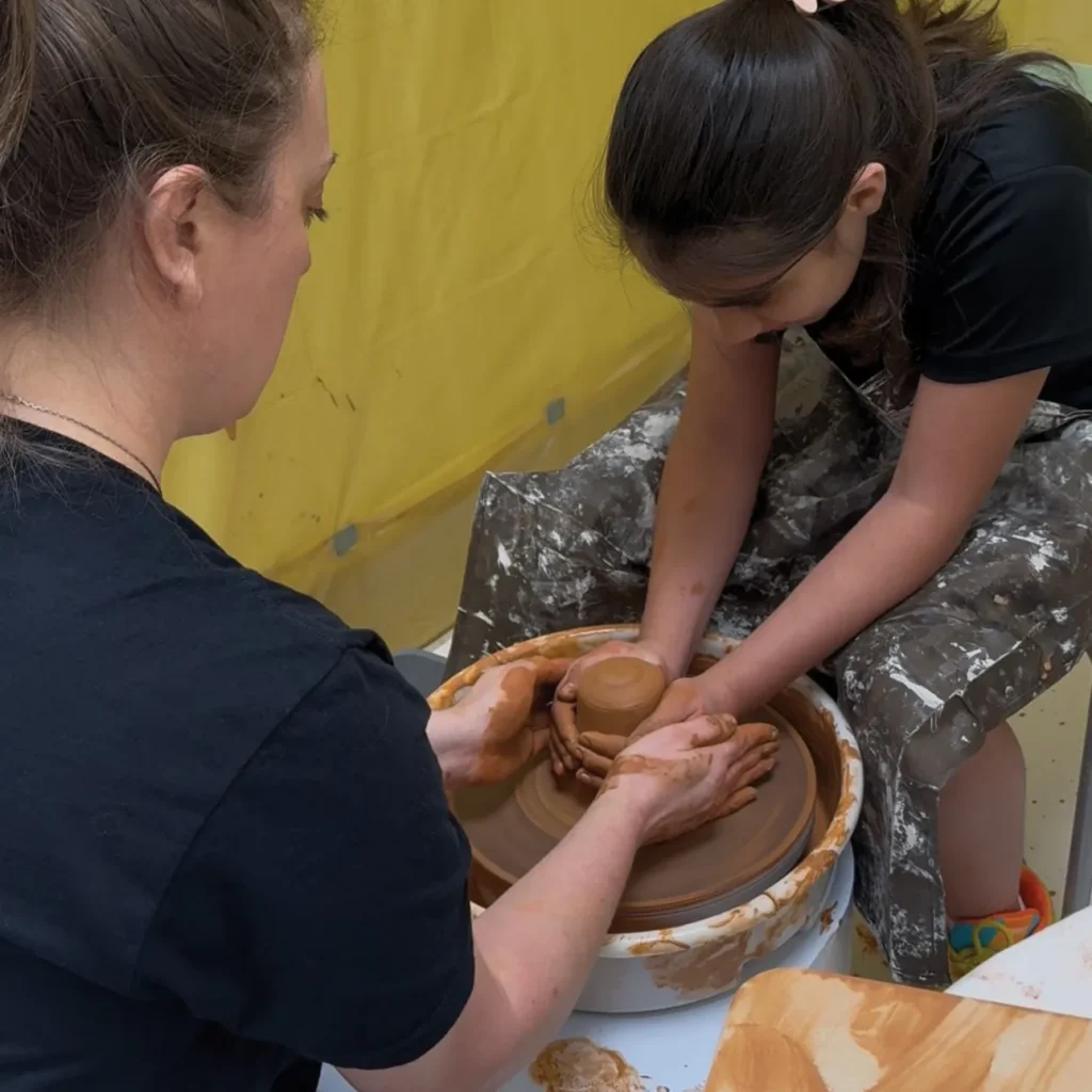 A child and an adult work together on a pottery wheel