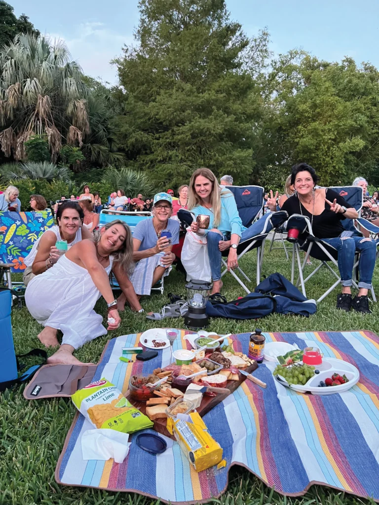 Happy people sitting on the grass around a blanket spread with food at a picnic