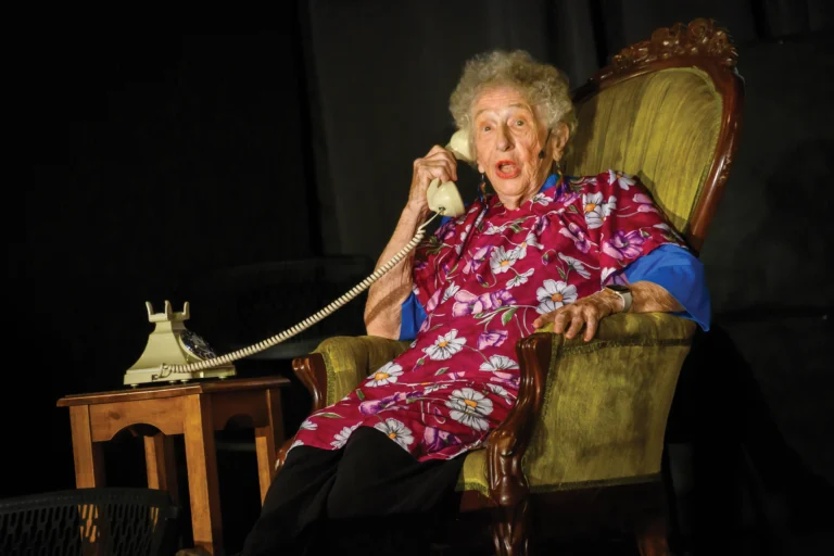 An elderly woman sitting in a chair holding a telephone