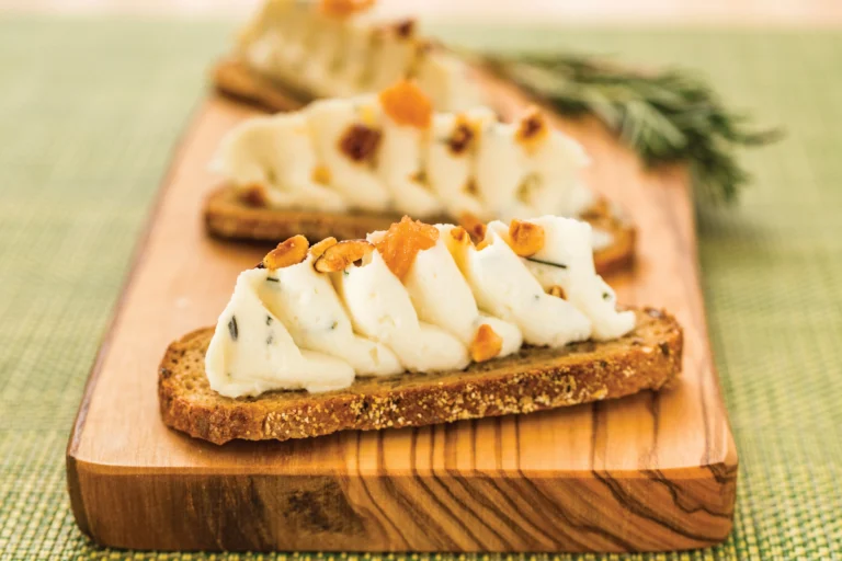 Two slices of toast topped with piped chèvre and candied hazelnuts on a wooden board