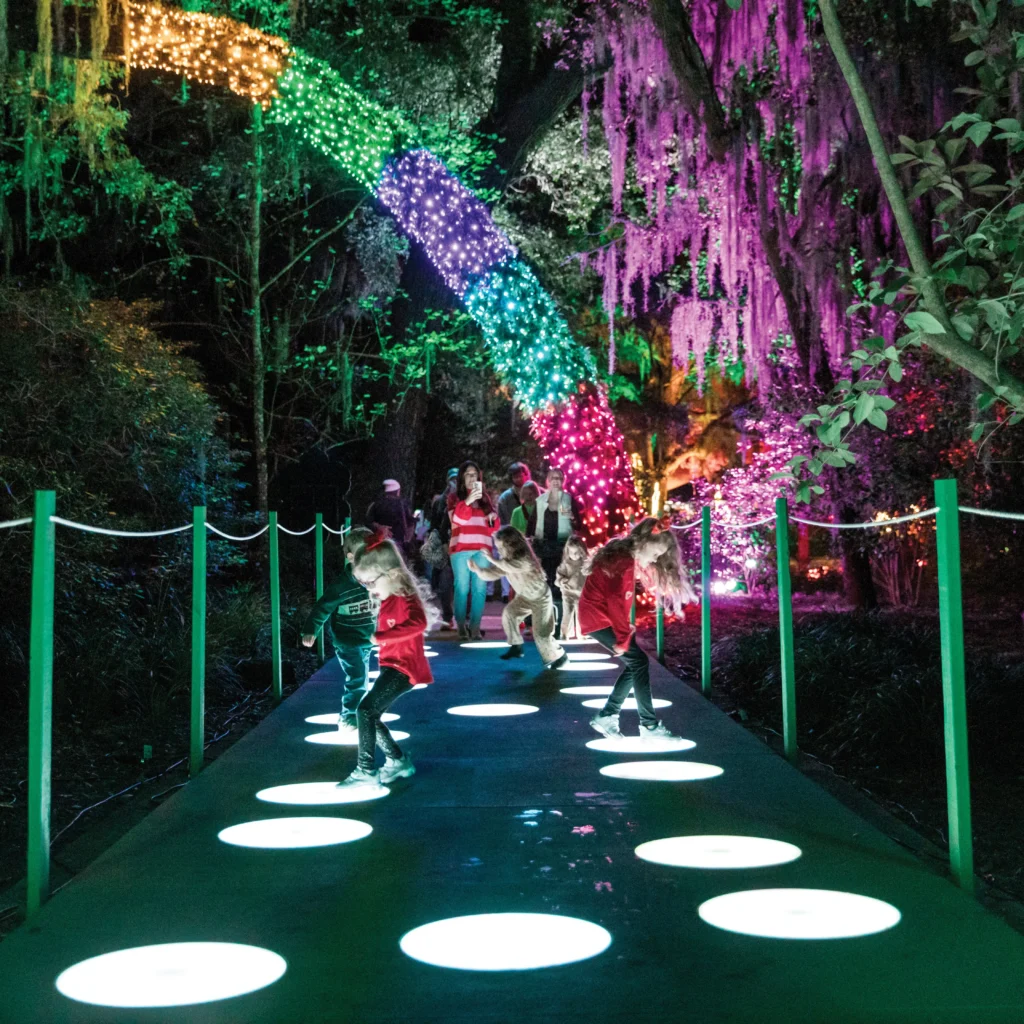 Children hopping across glowing circles on a garden path under a rainbow light arch
