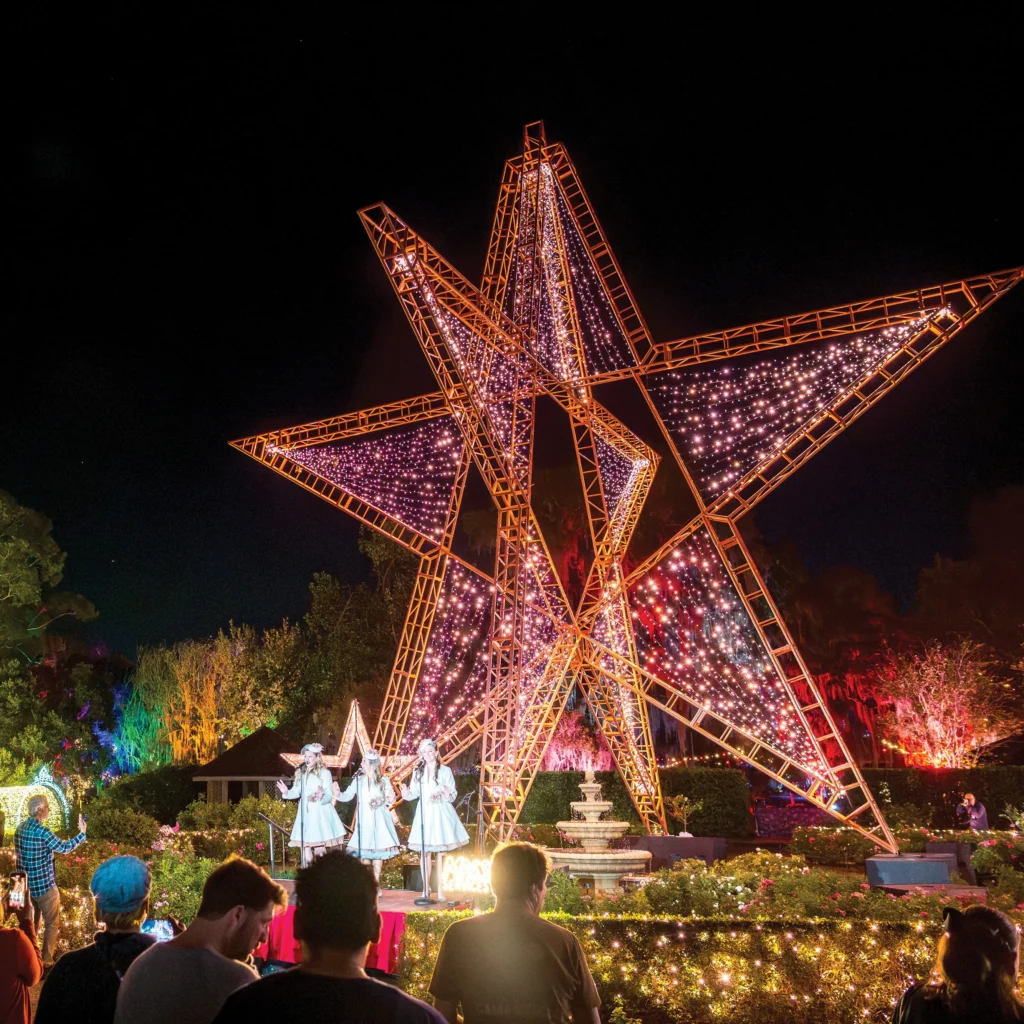 Giant illuminated star sculpture above singers in white performing for a crowd at Leu Gardens