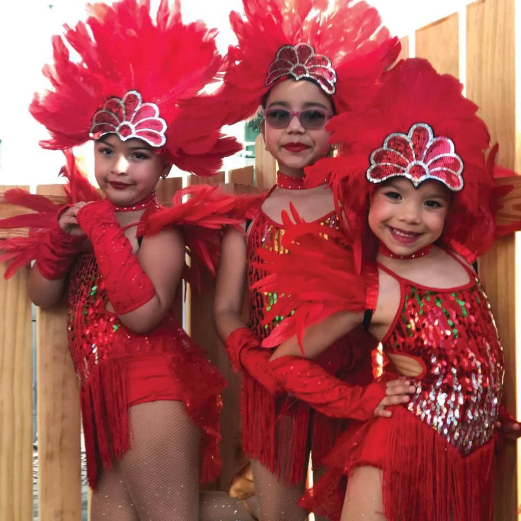 Three young dancers in red sequined costumes and feathered headdresses