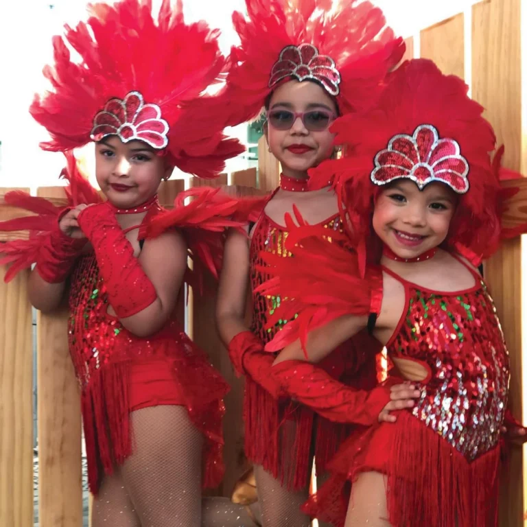 Three young dancers in red sequined costumes and feathered headdresses