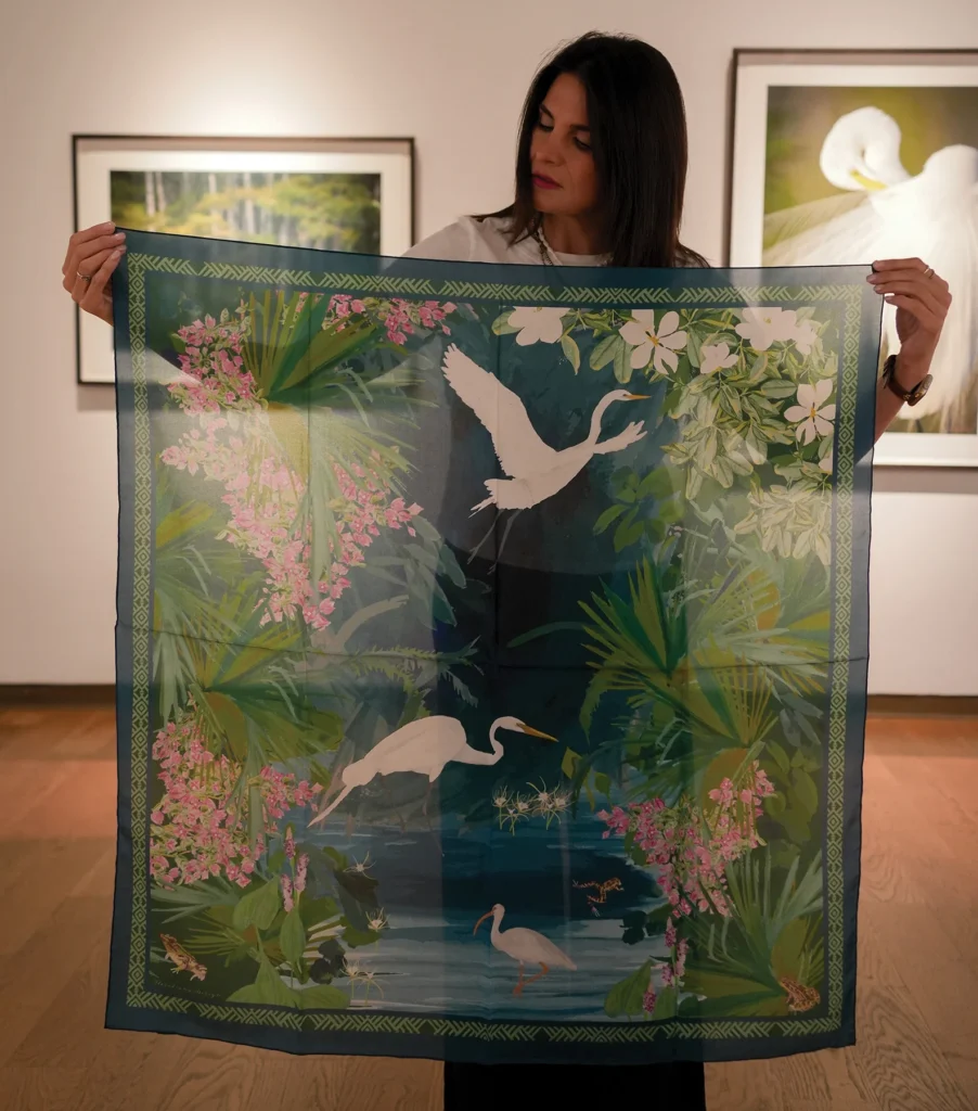 Woman holding up a silk scarf printed with egrets and tropical plants