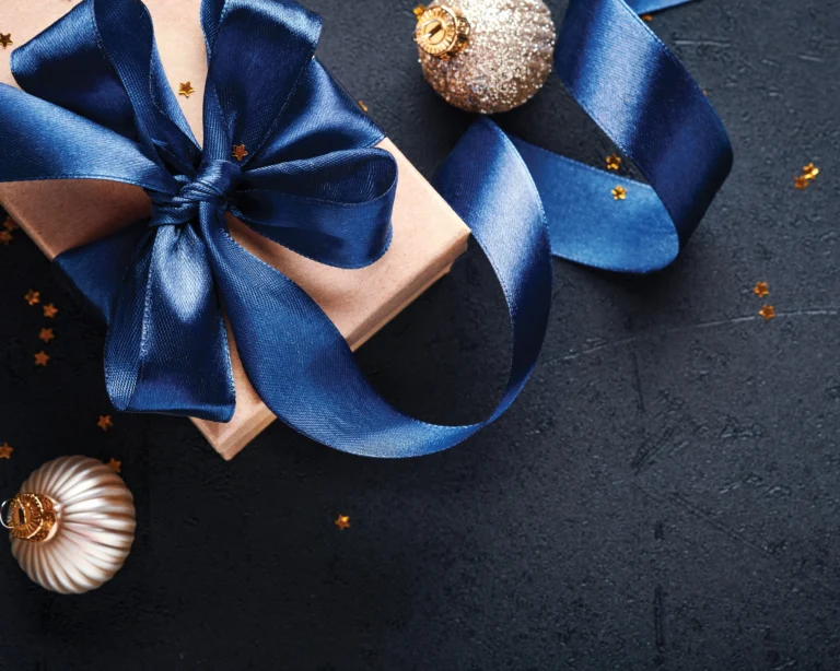 Wrapped holiday gift tied with a blue satin ribbon beside silver ornaments on a dark background