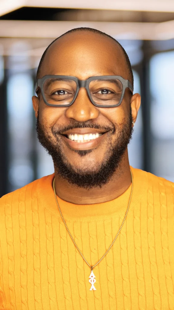 Jaylen Christie smiling in glasses and an orange sweater