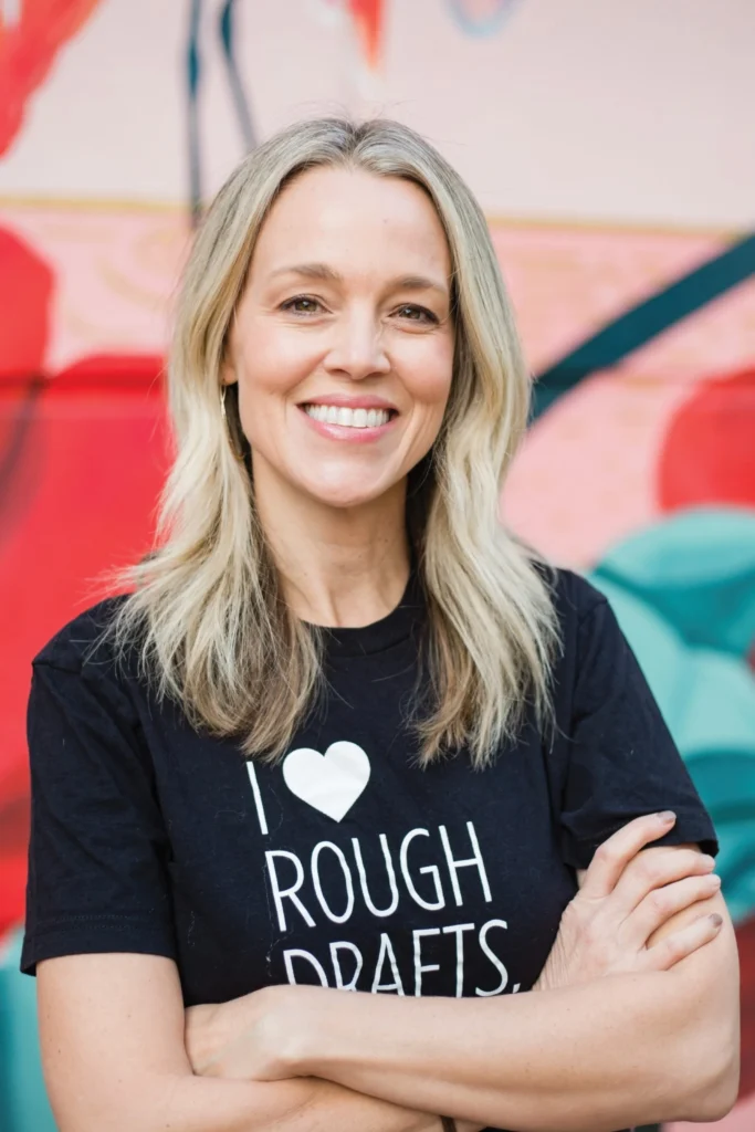 Julia Young smiling with arms crossed, wearing an I Love Rough Drafts T-shirt