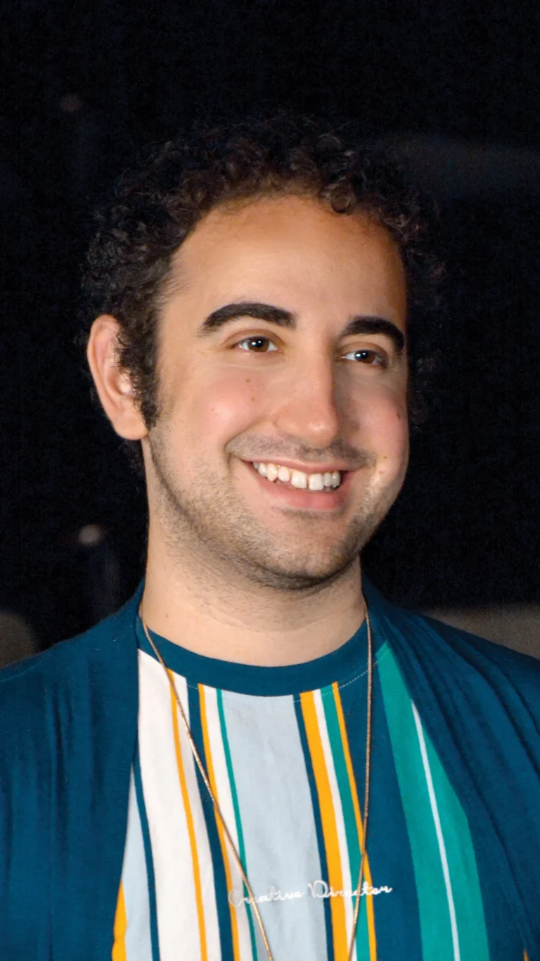 Max Pinsky smiling in a teal jacket and striped shirt